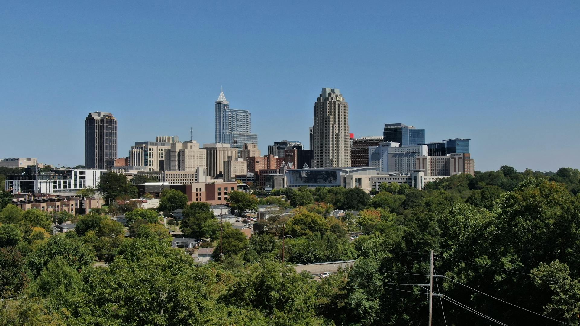 Raleigh, NC skyline featuring modern architecture and lush greenery on a clear day.