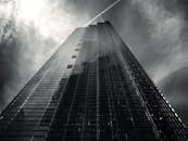 黑白照片中，一座高耸的摩天大楼矗立，云层和痕迹引人注目