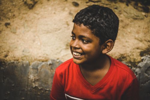Free A cheerful young boy in a red shirt smiling warmly against a textured wall background. Stock Photo