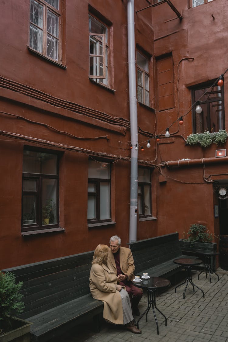 Couple Sitting On A Bench Beside A Building