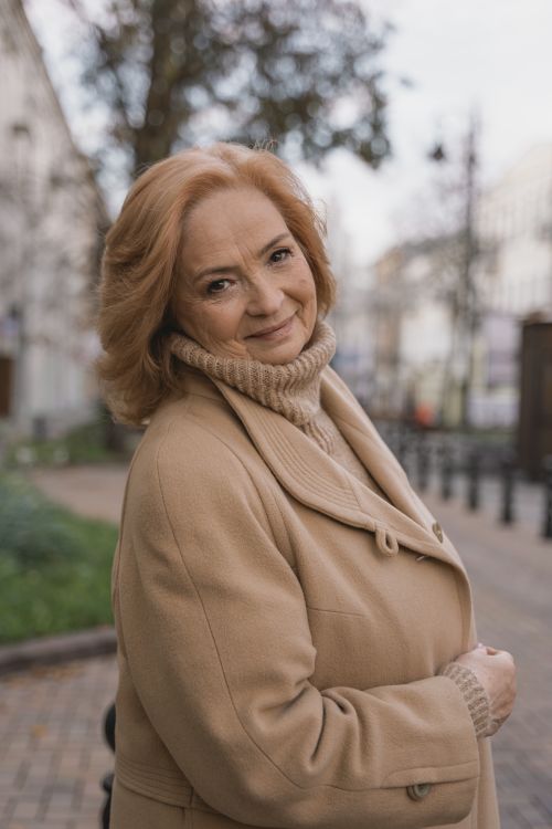 Free Smiling senior woman in beige coat and turtleneck enjoying a stroll outdoors in fall. Stock Photo