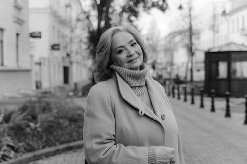 Free A stylish senior woman standing on a city sidewalk, smiling warmly in grayscale photography. Stock Photo