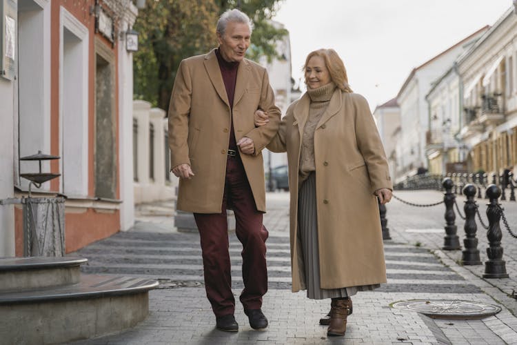 An Elderly Man And A Woman Walking On The Sidewalk