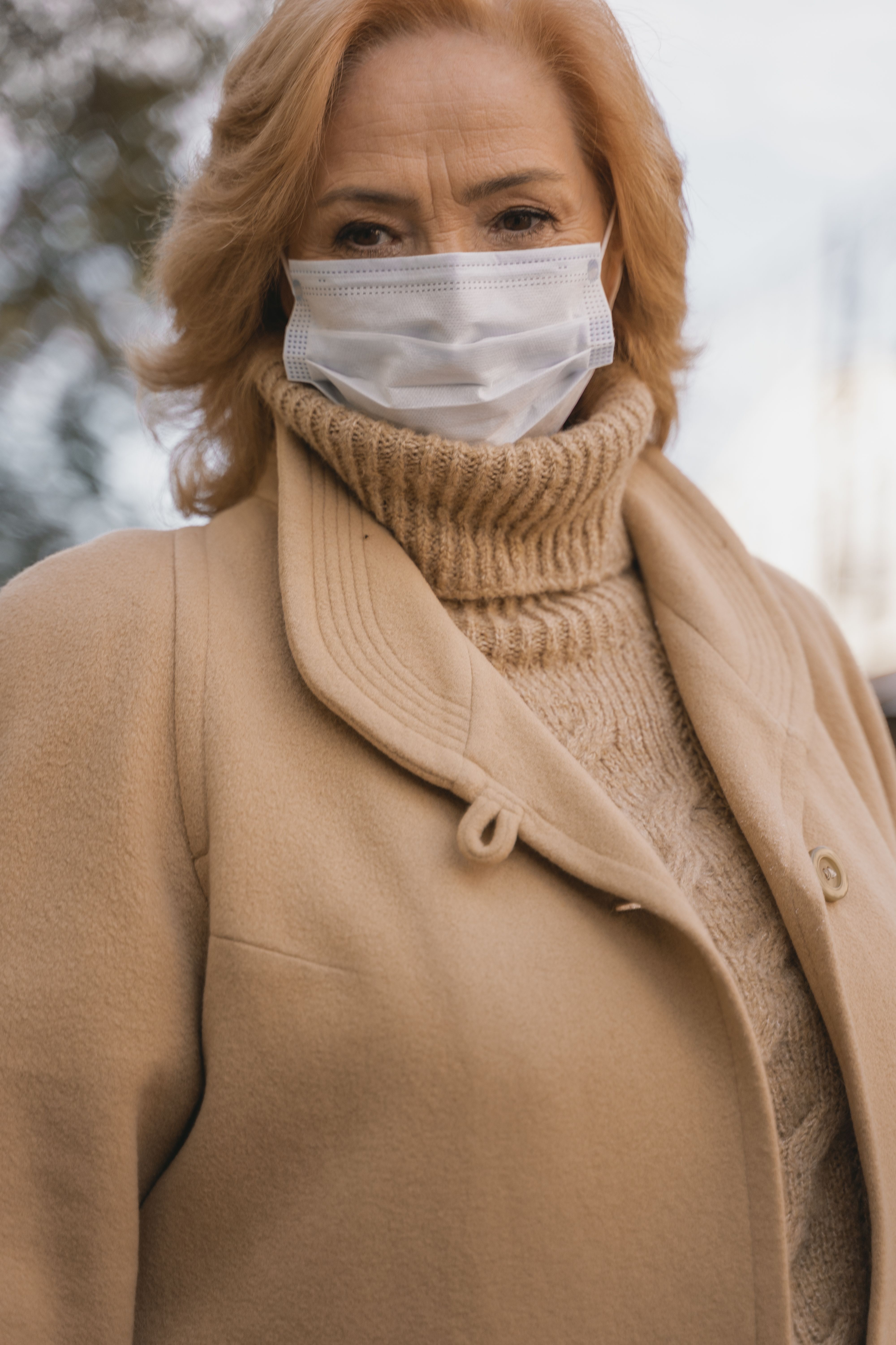 一位穿着棕色外套和高领毛衣的女士戴着口罩在户外