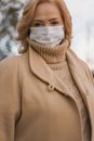 一位穿着棕色外套和高领毛衣的女士戴着口罩在户外
