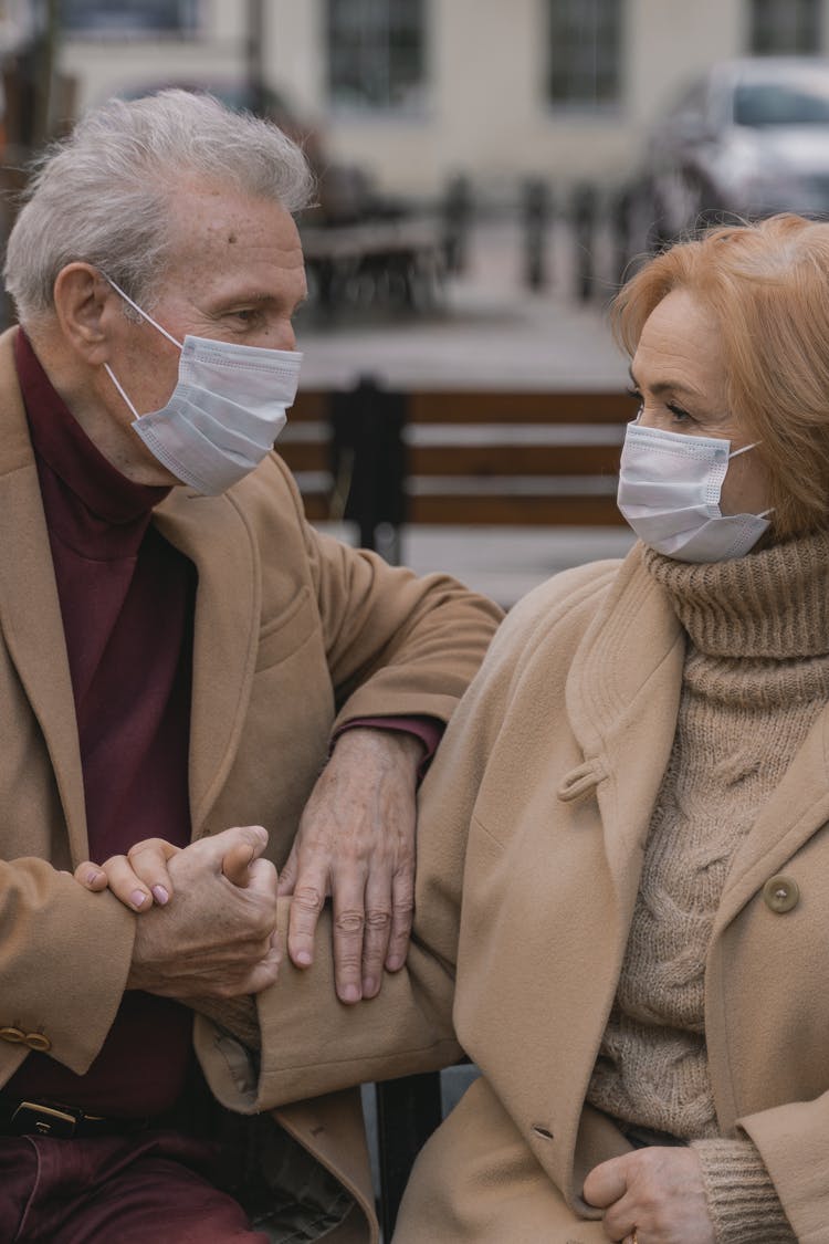 An Elderly Couple Sitting On The Bench Holding Hands