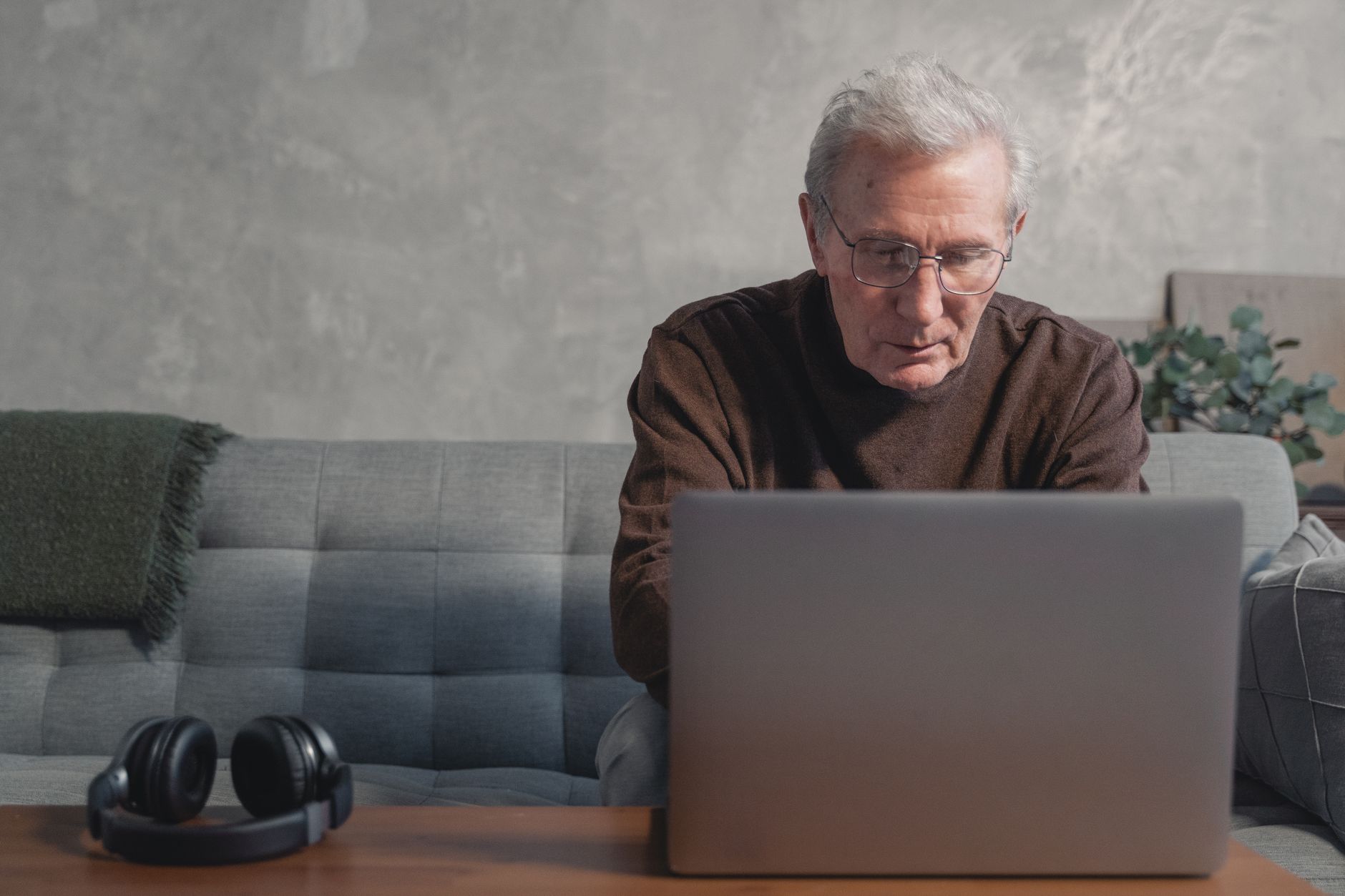 Elderly man focused on using a laptop on a couch, showing engagement with technology.