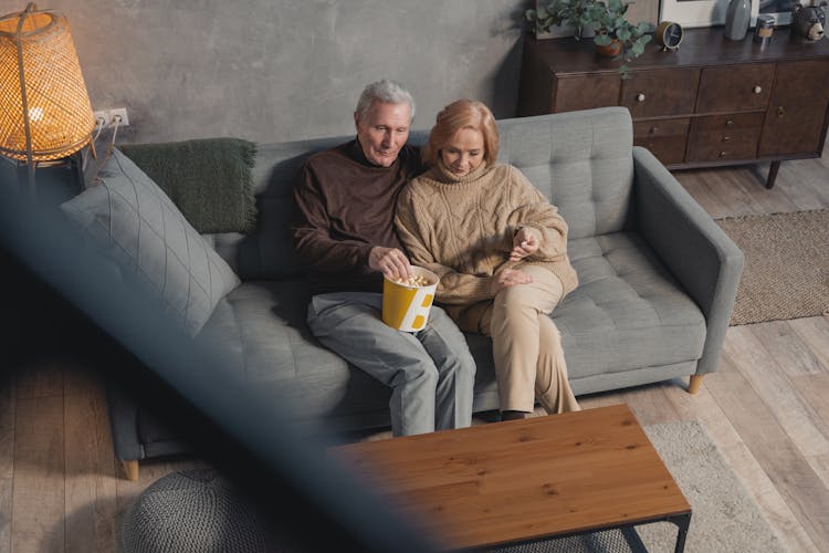 Man And Woman Sitting On Couch With A Bucket Of Popcorn