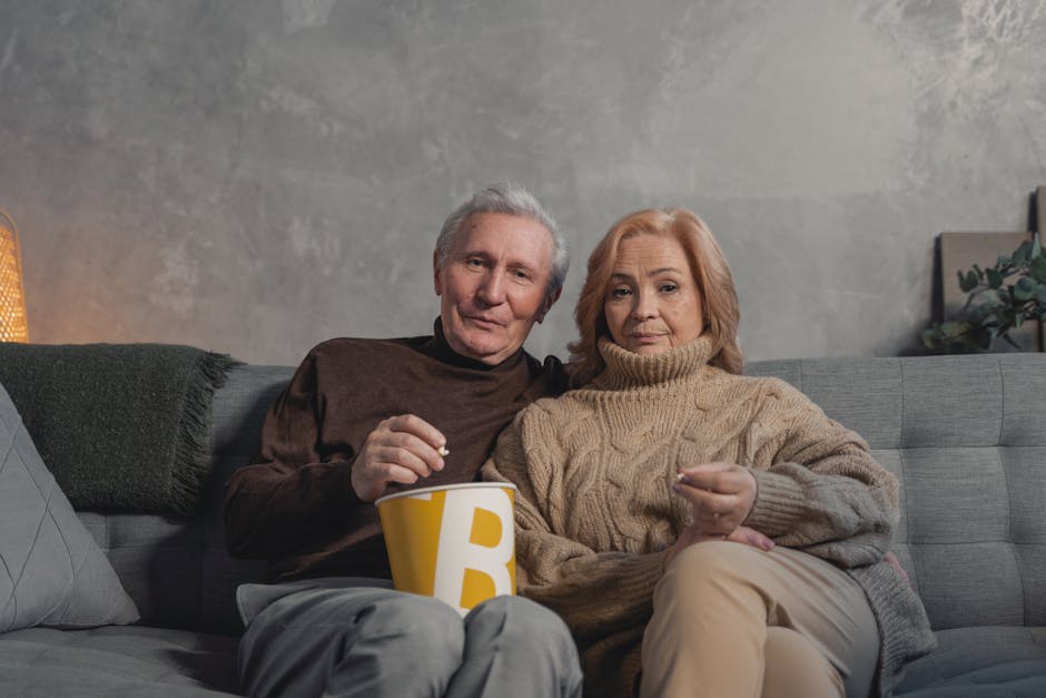 Elderly couple enjoying a cozy evening at home, watching TV with popcorn.