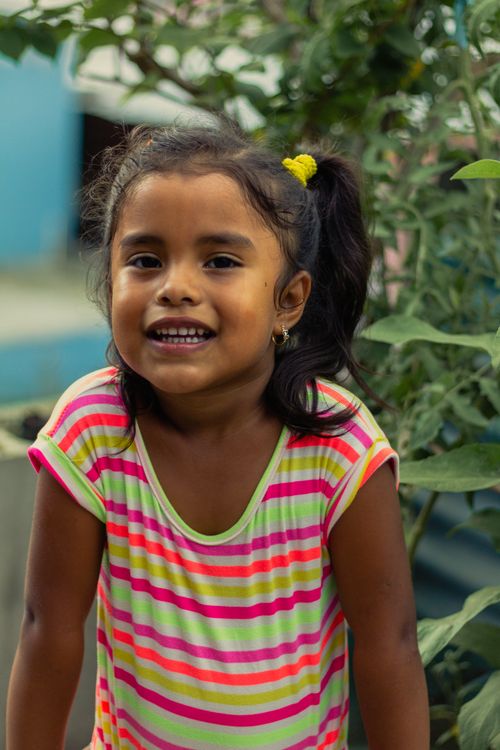 Free A cheerful young girl with a ponytail smiles brightly, standing outdoors in vibrant attire. Stock Photo
