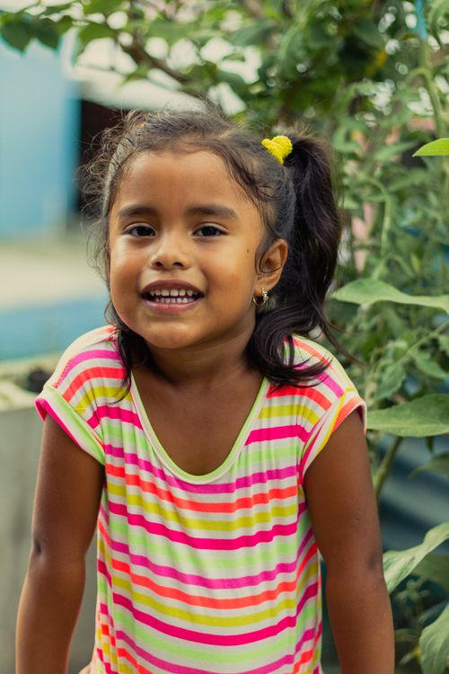 Free A happy child with a ponytail smiling brightly outdoors in vibrant summer clothing. Stock Photo