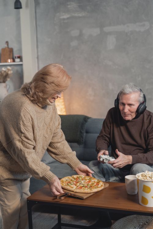 Free Senior couple relaxing indoors with pizza and video games, capturing a cozy lifestyle moment. Stock Photo
