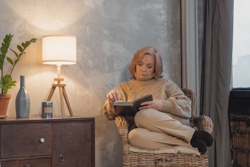 Woman Reading a Book While Sitting on a Chair