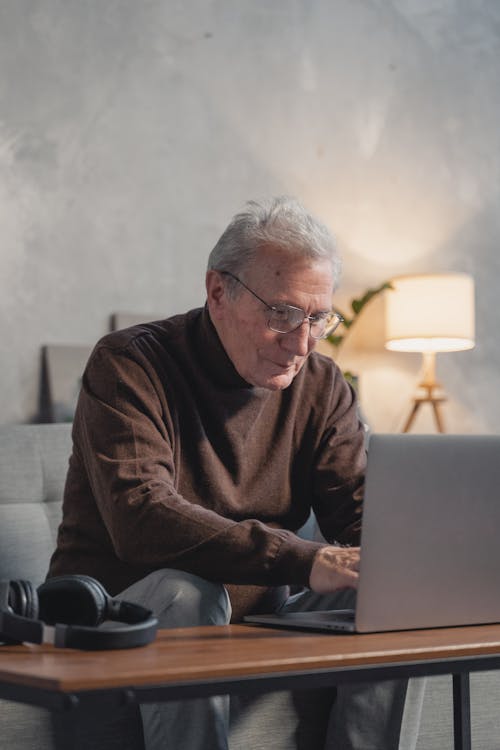 Man in Brown Sweater Sitting on Couch Using Laptop Computer