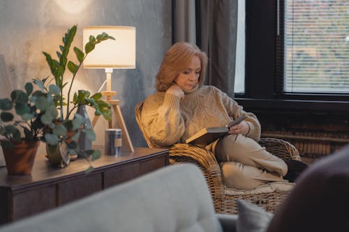 Eldelry Woman in Sweater Sitting on Armchair and Reading Book
