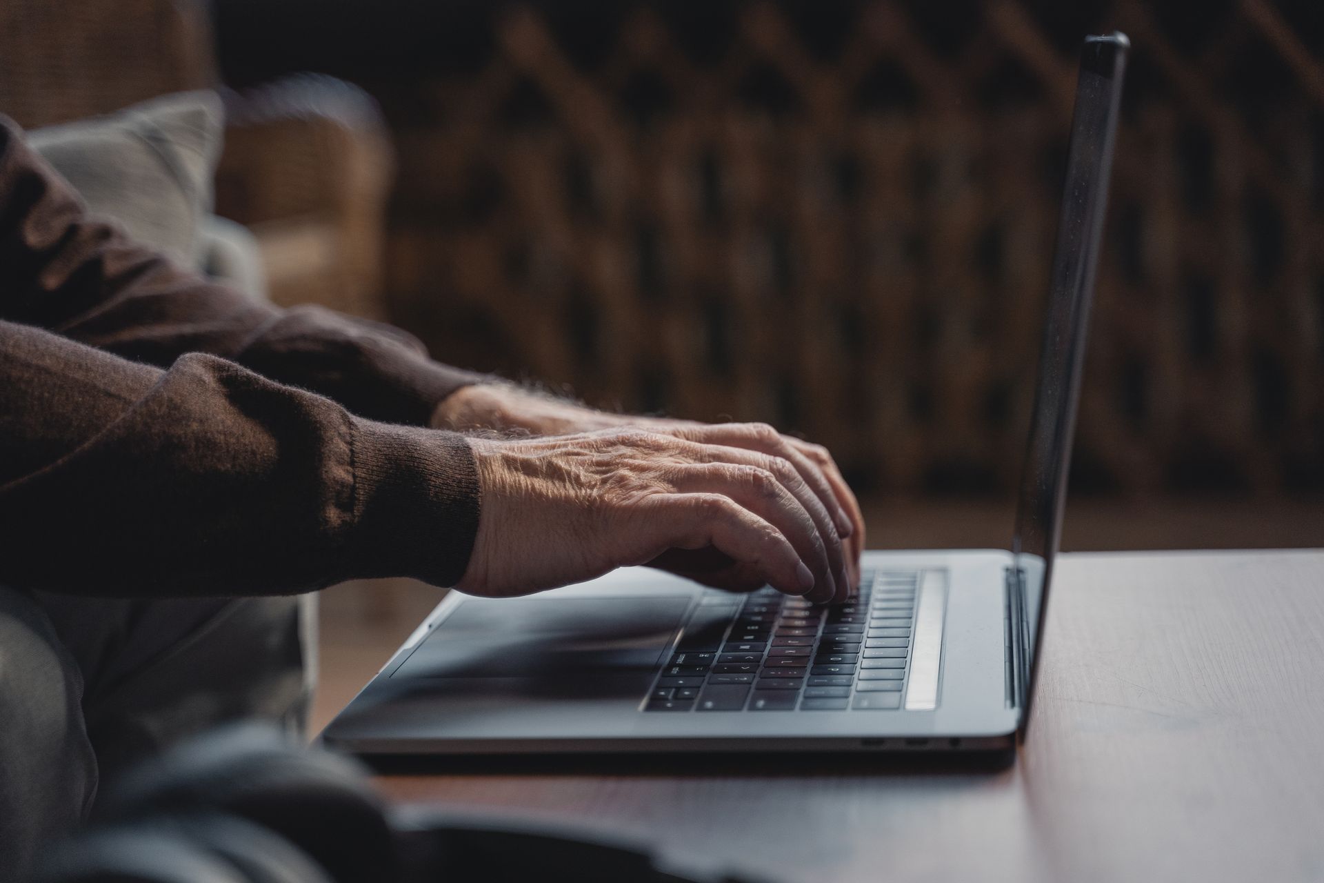 Senior adult typing on laptop indoors, showcasing technology use by older generation in a warm setting.