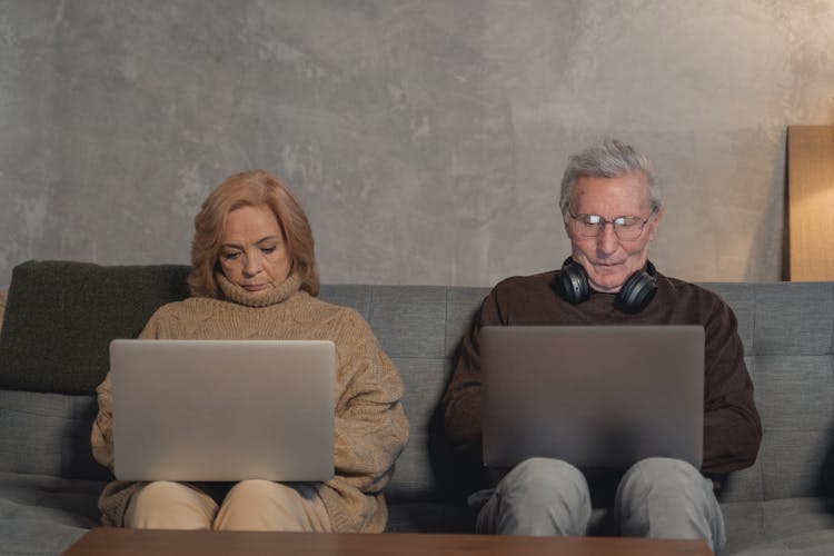 Elderly Couple Sitting On Sofa Busy Using Laptops