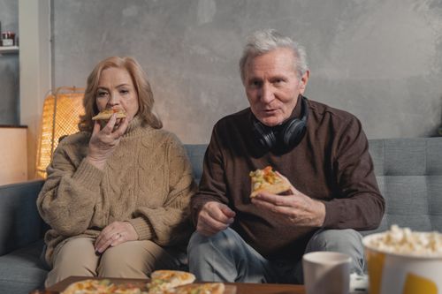 Free Elderly couple shares pizza and leisure time on a comfortable sofa, embodying love and togetherness. Stock Photo