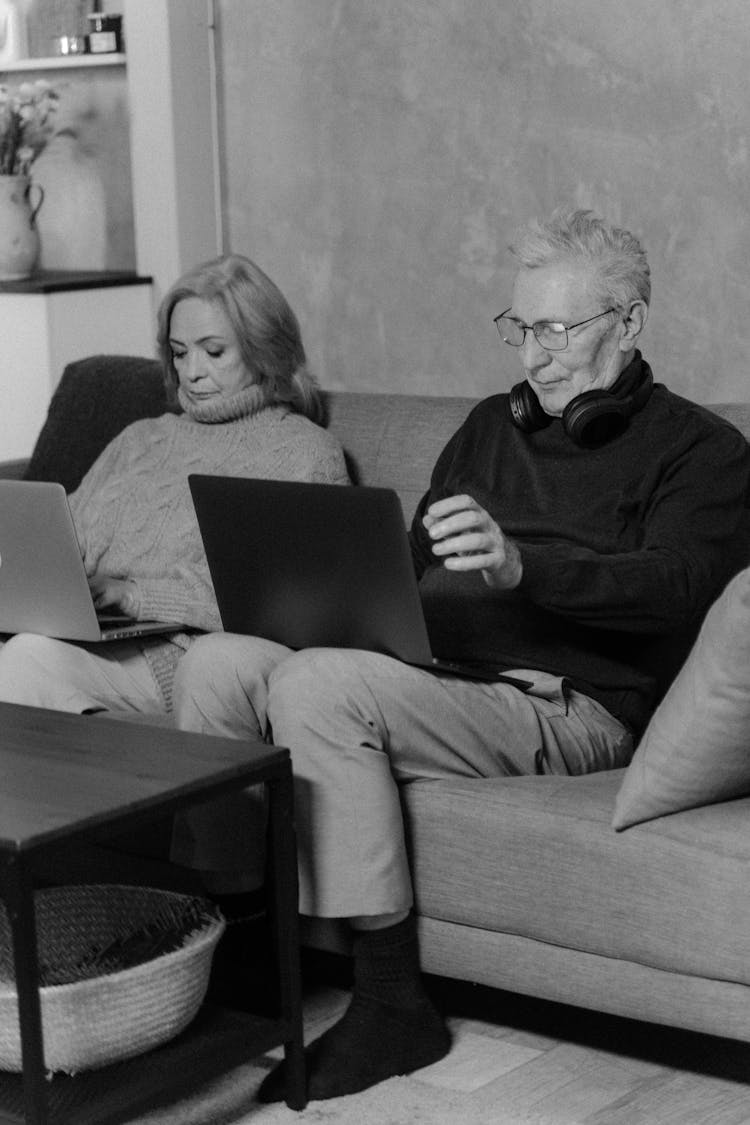 Elderly Man And Woman Sitting On Couch Using Laptops