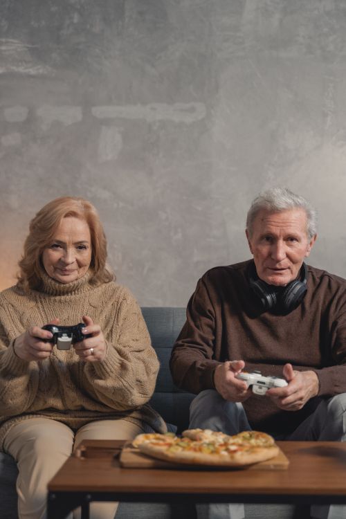 Free Senior couple playing video games and enjoying pizza, embracing fun and togetherness at home. Stock Photo