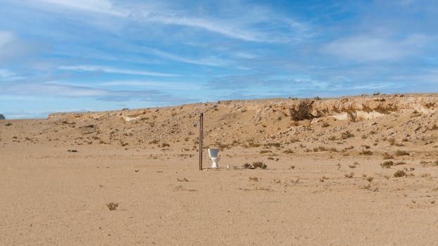 贫瘠的沙漠中，一个孤立的马桶立在明亮的蓝天下