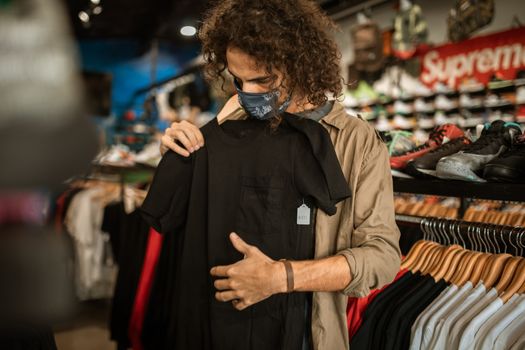 一个男人戴着面具在室内时装店挑选衣服