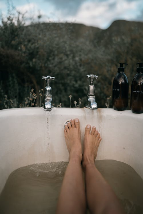 Photo of a Person's Feet Near Silver Faucets
