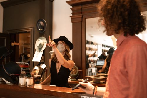 Free A fashionable woman assists a customer in a chic hat boutique, highlighting style and shopping experience. Stock Photo