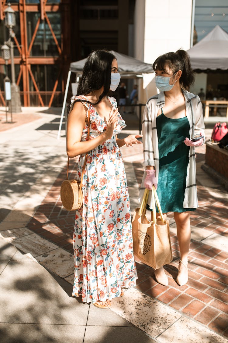 Two Women Carrying Bags Standing While Talking Outside