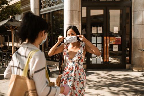 Free Two women in floral dresses meet outdoors, adjusting face masks during a sunny day. Stock Photo