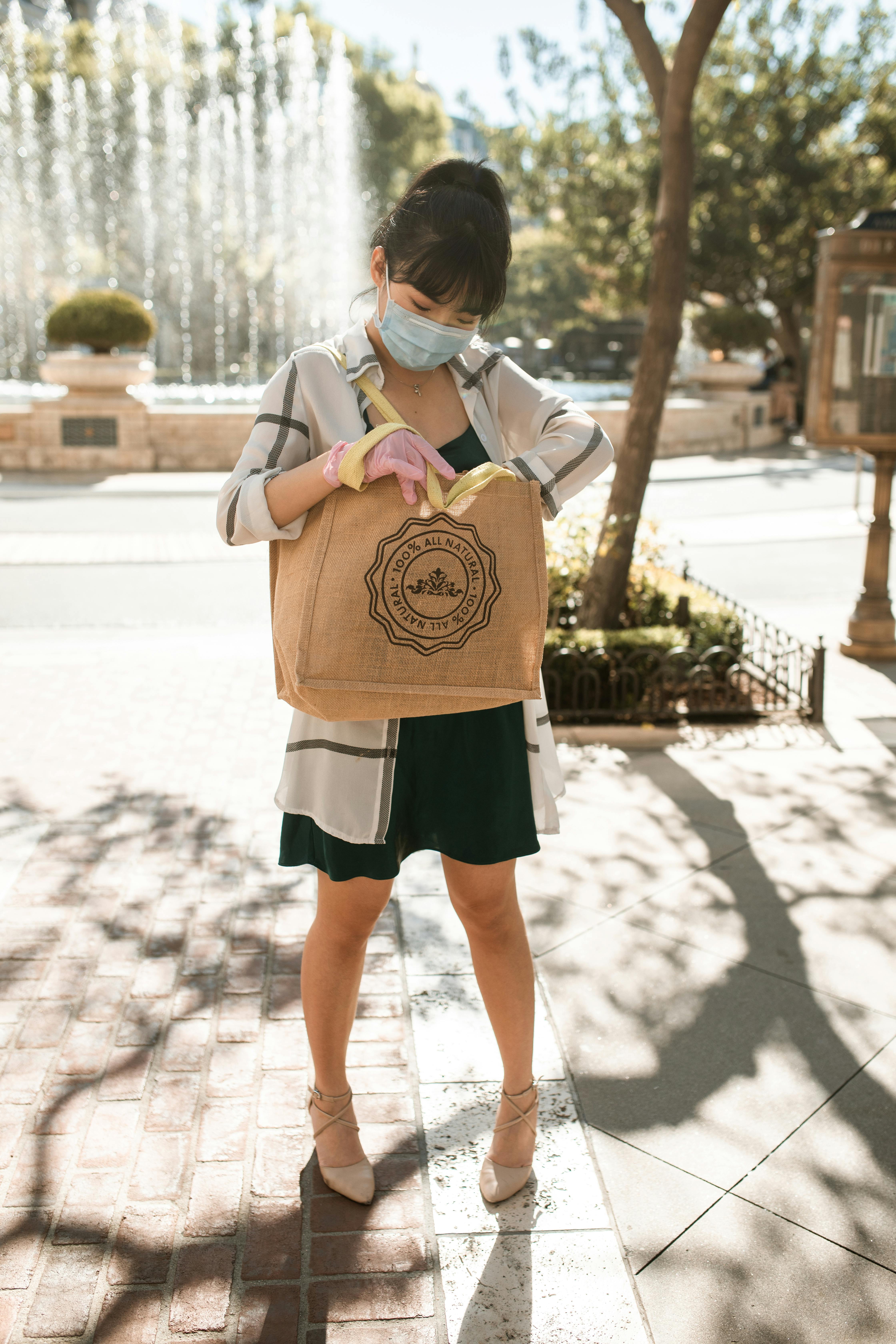 疫情期间，一位戴着口罩和手套、提着环保袋的亚洲妇女在外购物