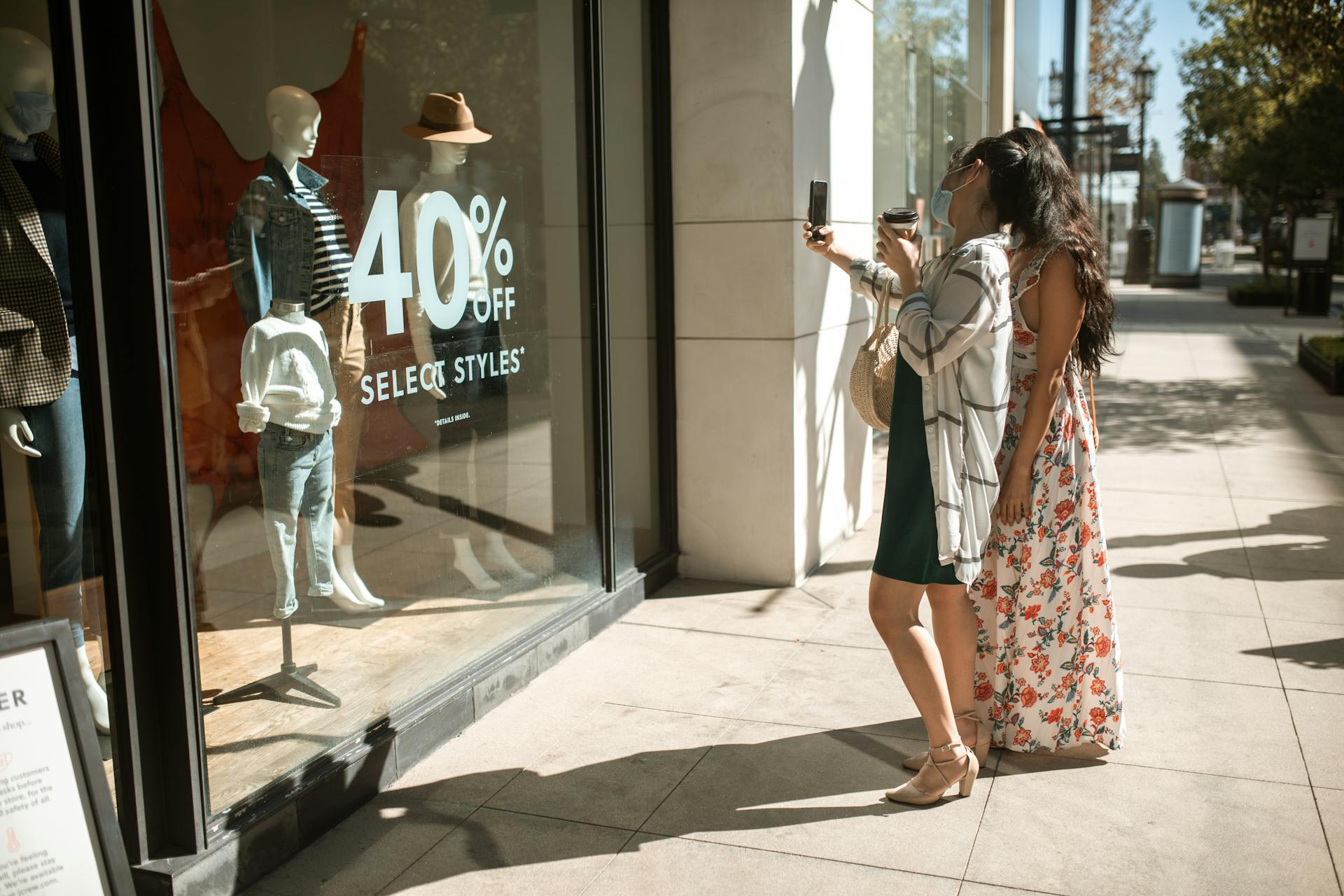 Two women taking photos of a boutique window display with a 40% off sale sign.