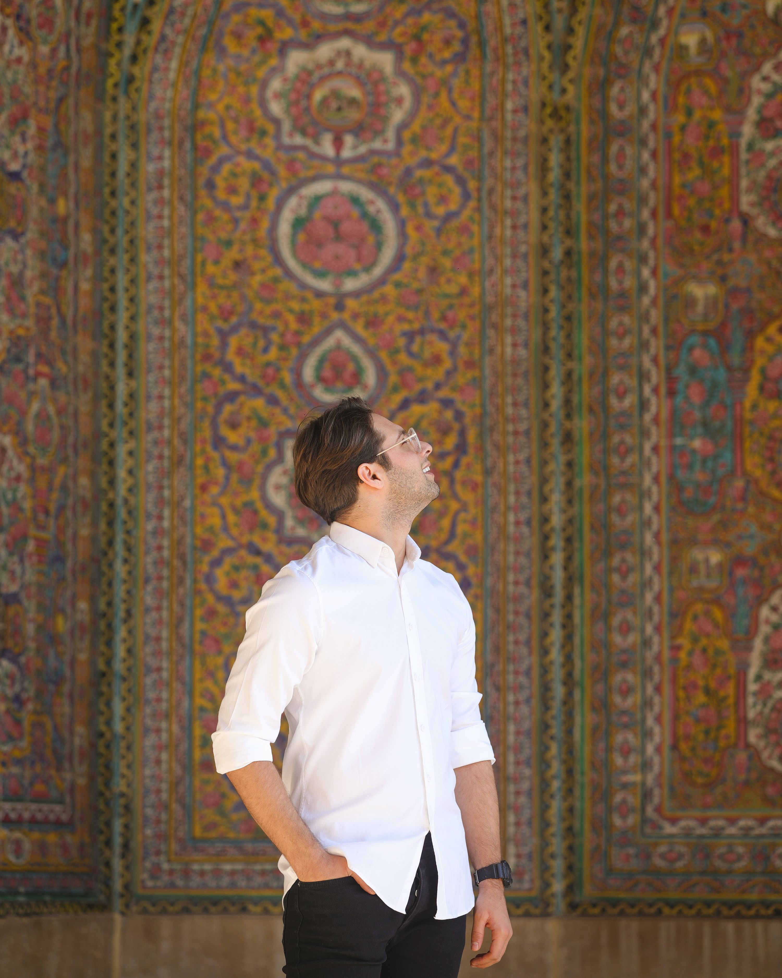 Man in white shirt admires ornate Persian wall in Tehran Iran.