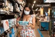 一位年轻女子戴着口罩在商店的过道里选购花裙