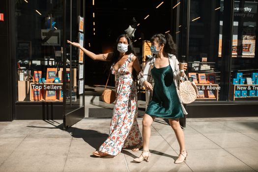 两名妇女戴着口罩在明亮的日光下安全地户外购物