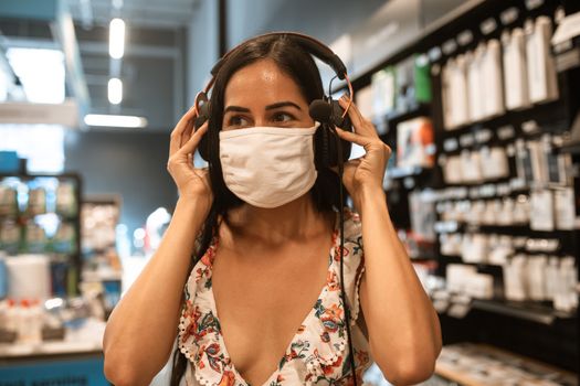一名妇女在商店里戴着口罩试戴耳机，展现了现代购物的场景