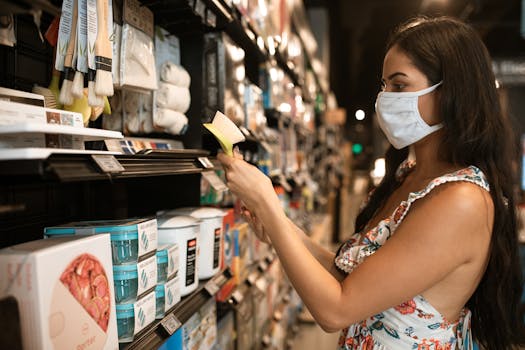 A woman in a floral dress shops for household goods while wearing a face mask in a store.