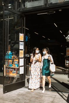 阳光明媚的日子里，两名戴着口罩的妇女购物后离开了商店