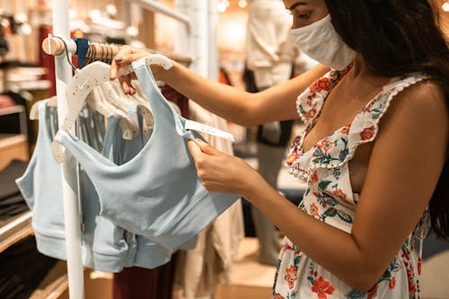 Woman in Floral Dress Looking at a Price Tag of Blue Top on Hanger