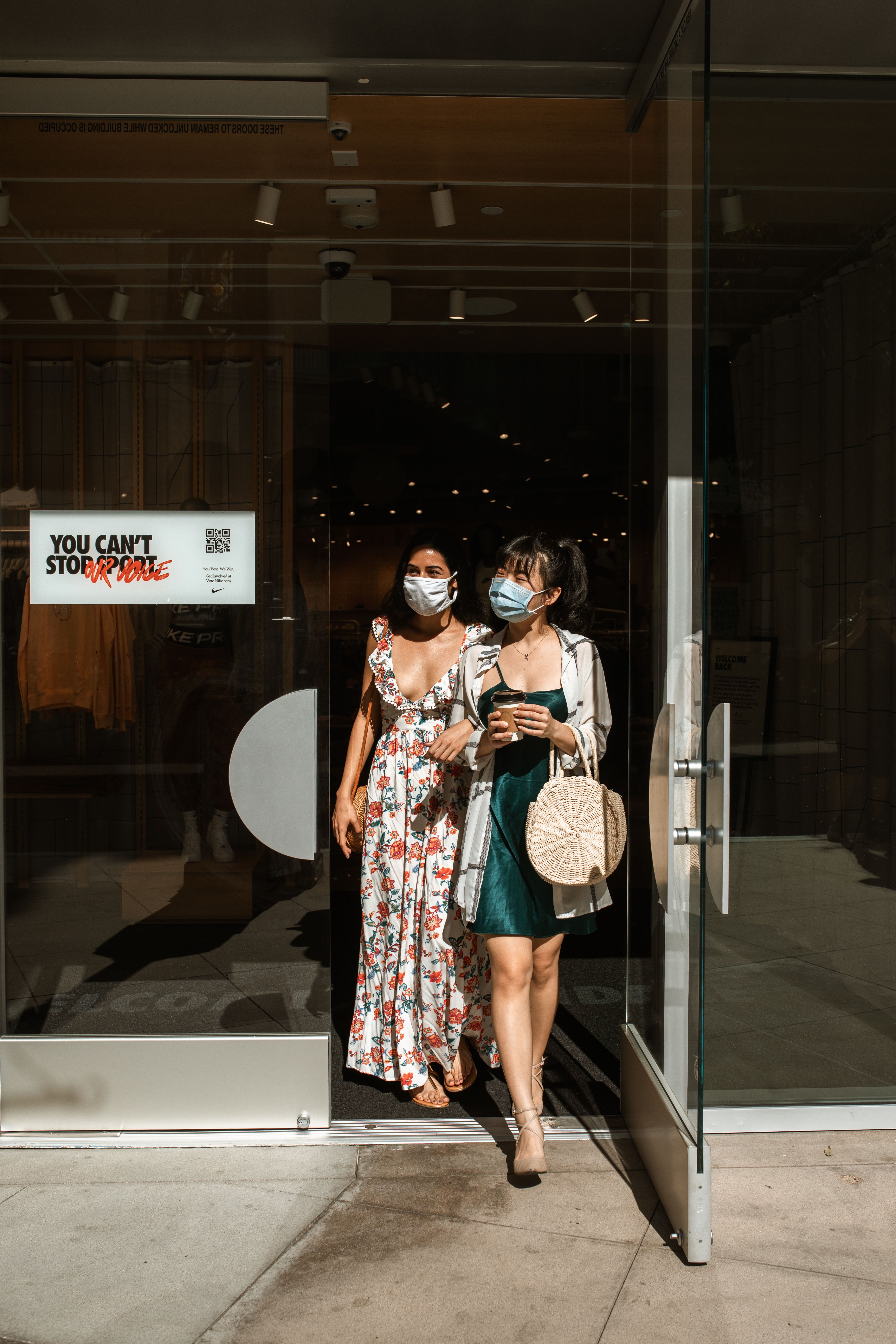 两名穿着时髦的女性戴着口罩走出商店，这代表着大流行时代的购物