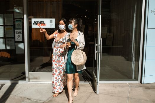 两名戴着口罩的妇女离开了那个充满活力的购物区的商店
