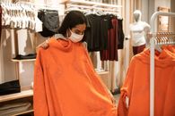 一个女人在服装店检查橙色毛衣，她戴着口罩