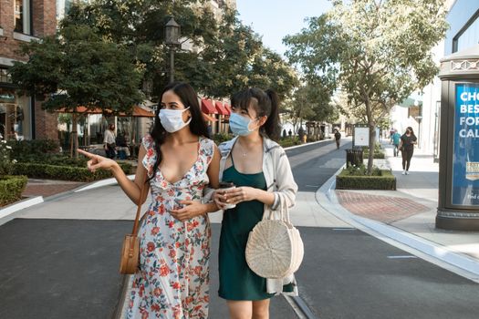 两名妇女戴着口罩在户外购物，拥抱新的生活方式