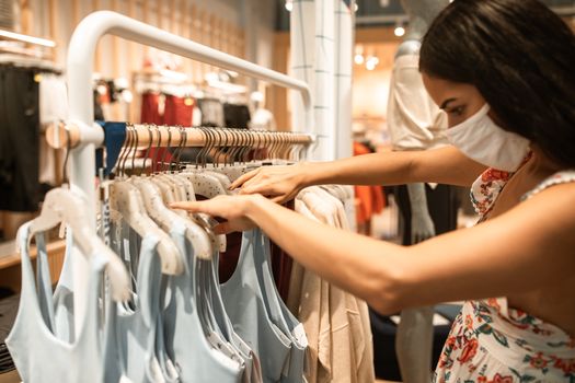 一名女子戴着口罩在商店买衣服，这反映了疫情下的新常态