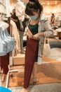一名妇女戴着口罩，在一家光线充足的零售店里买衣服