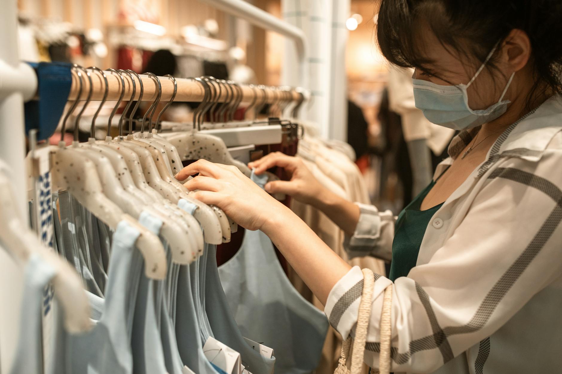 Woman wearing a face mask shopping for apparel indoors, emphasizing safety and fashion.