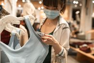 商店里，一名女子戴着口罩检查衣服标签，适应了新的购物常态