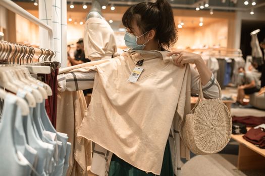 一名妇女戴着口罩购买衣服，体现了疫情下生活方式的变化