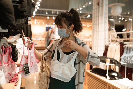 在零售店，戴着面具的女人正挑选运动胸罩，以适应新常态