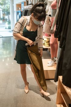 一名戴口罩的妇女在服装店里检查一条棕色裤子